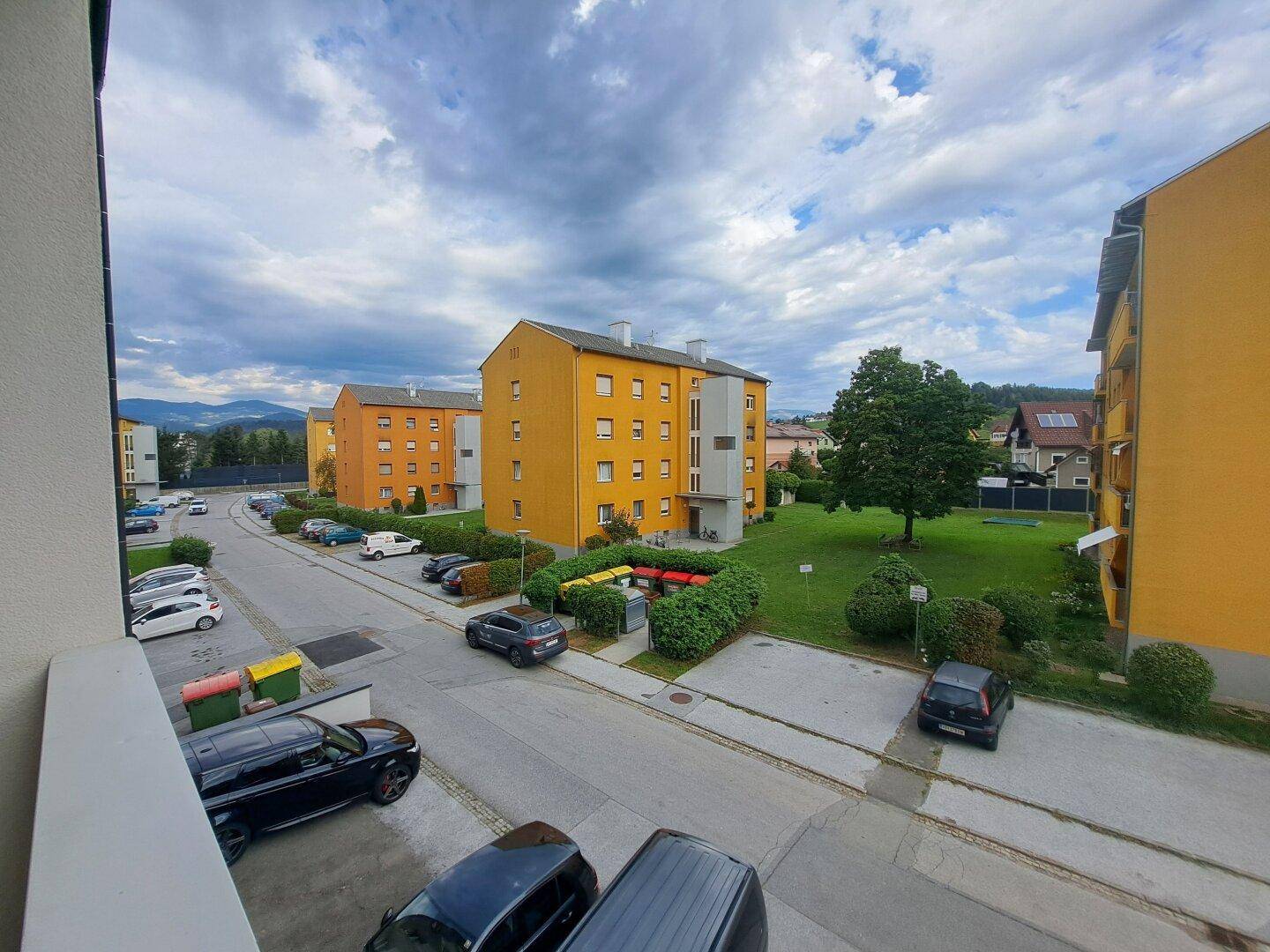 Ausblick vom Balkon auf die Straße, Parkplätze und grüne Flächen zwischen den Gebäuden.
