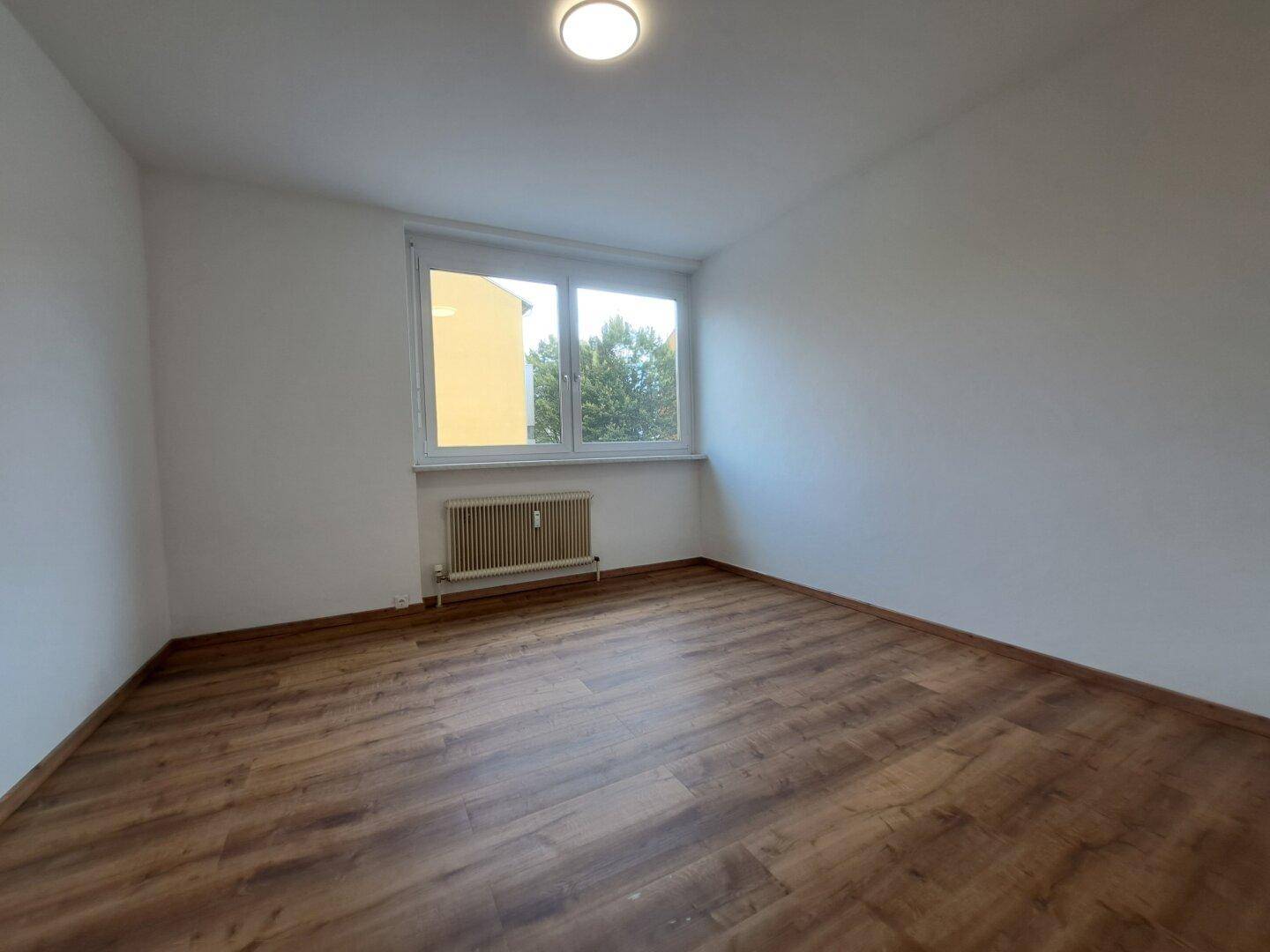 Helles, leeres Zimmer mit Laminatboden und einem Fenster, bereit zur individuellen Gestaltung.