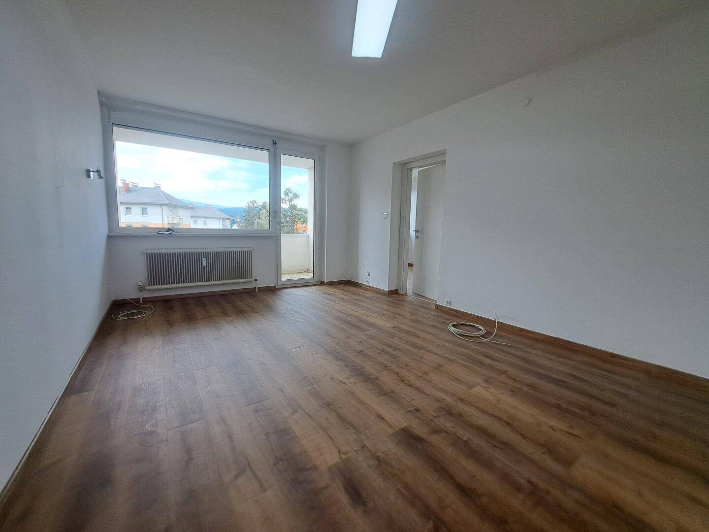Geräumiges Wohnzimmer mit Laminatboden und Zugang zu einem Balkon, hell und einladend.