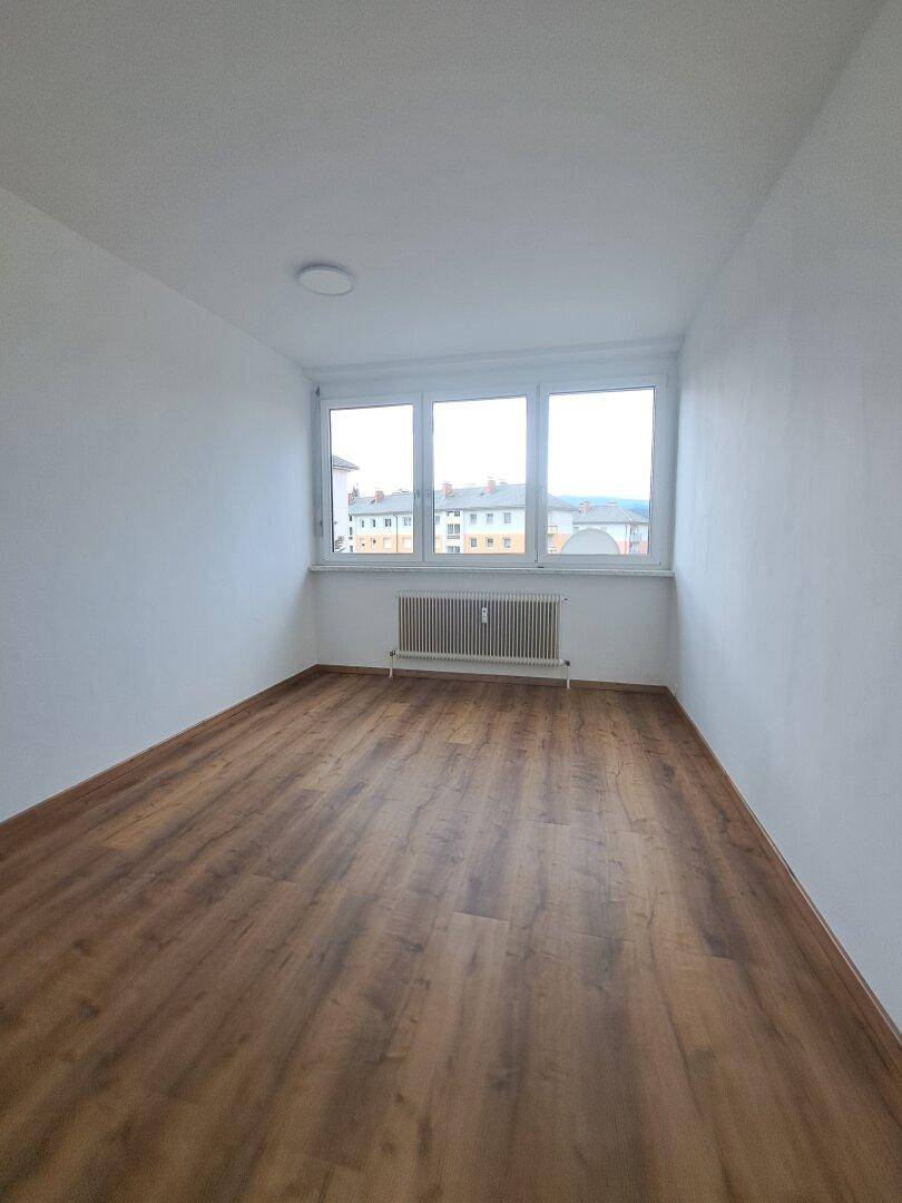 Freundliches Schlafzimmer mit Laminatboden, weißen Wänden und drei Fenstern für helle Atmosphäre.