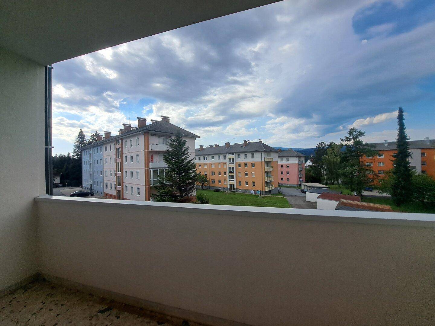 Weitblick vom Balkon auf eine Wohnsiedlung mit Bäumen und bewölktem Himmel.