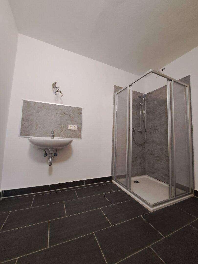 Modernes Badezimmer mit dunklen Fliesen, Waschbecken und einer Duschkabine mit Glaswänden.