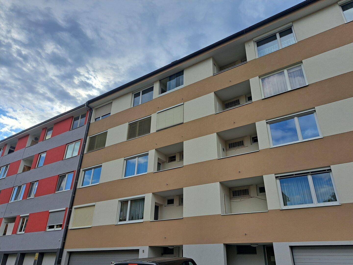 Fassade eines Mehrfamilienhauses mit vielen Fenstern und Balkonen in braun-beigen Farbtönen.