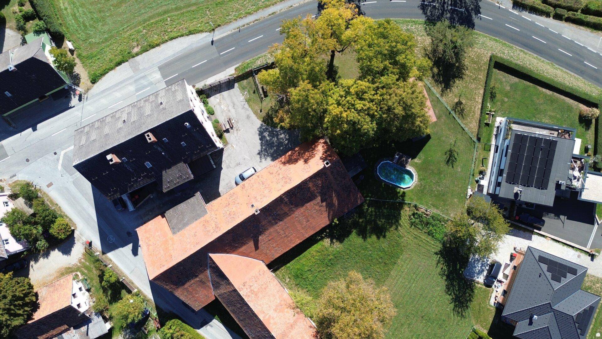 Vogelperspektive des Anwesens mit Hauptgebäude, L-förmigem Nebengebäude, kleinem Pool und umliegenden Grünflächen.