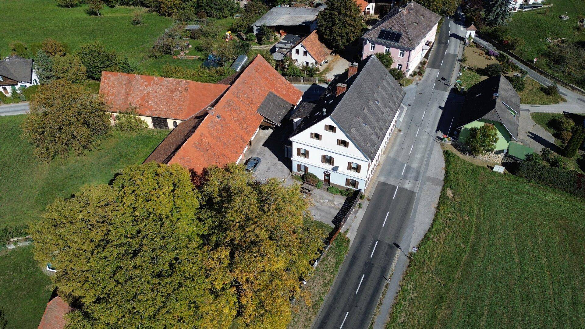 Luftaufnahme des weißen Hauptgebäudes mit braunen Fensterläden, dem roten Scheunendach und der ländlichen Umgebung.