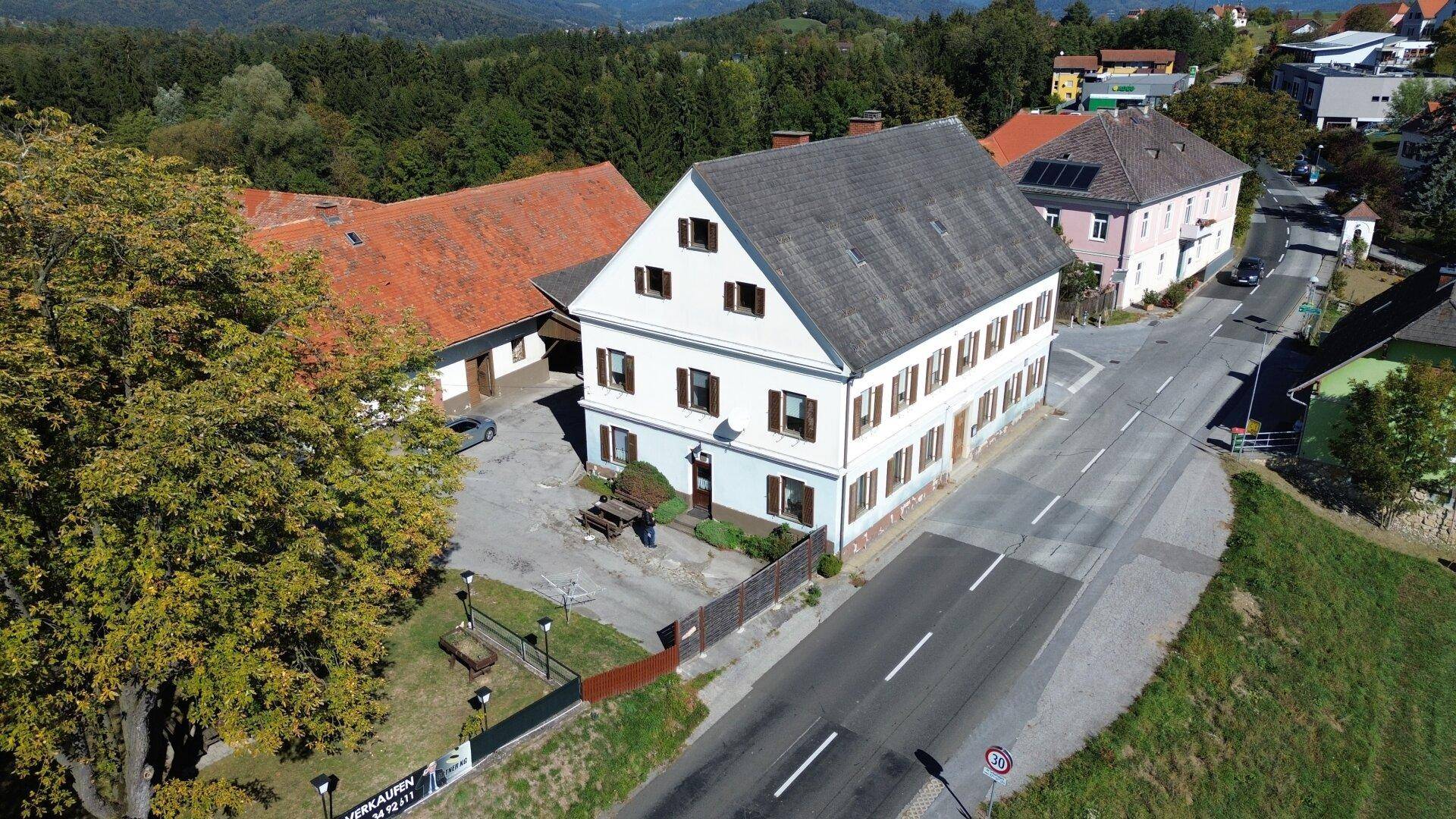Nahaufnahme aus der Luft eines traditionellen weißen Gebäudes mit braunen Fensterläden und einem grauen Dach neben einer Straße.