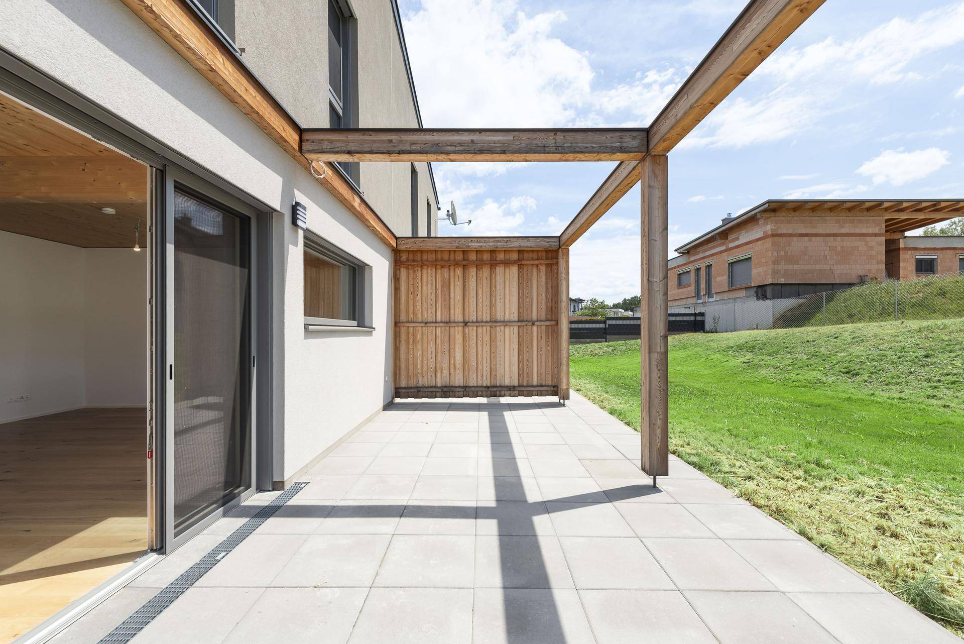 Sonniger Terrassenbereich mit Holzpergola und direktem Zugang zum Haus und Garten.