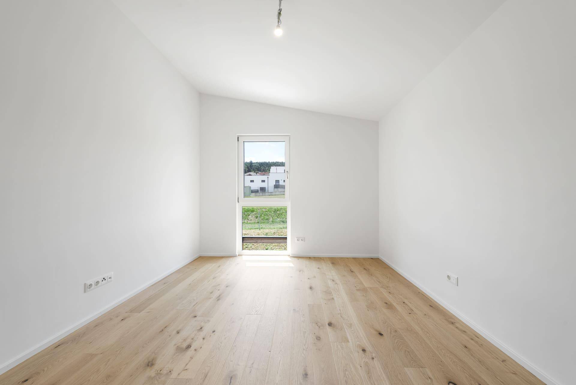 Helles Schlafzimmer mit Holzboden und einer Tür, die direkten Zugang ins Freie bietet.