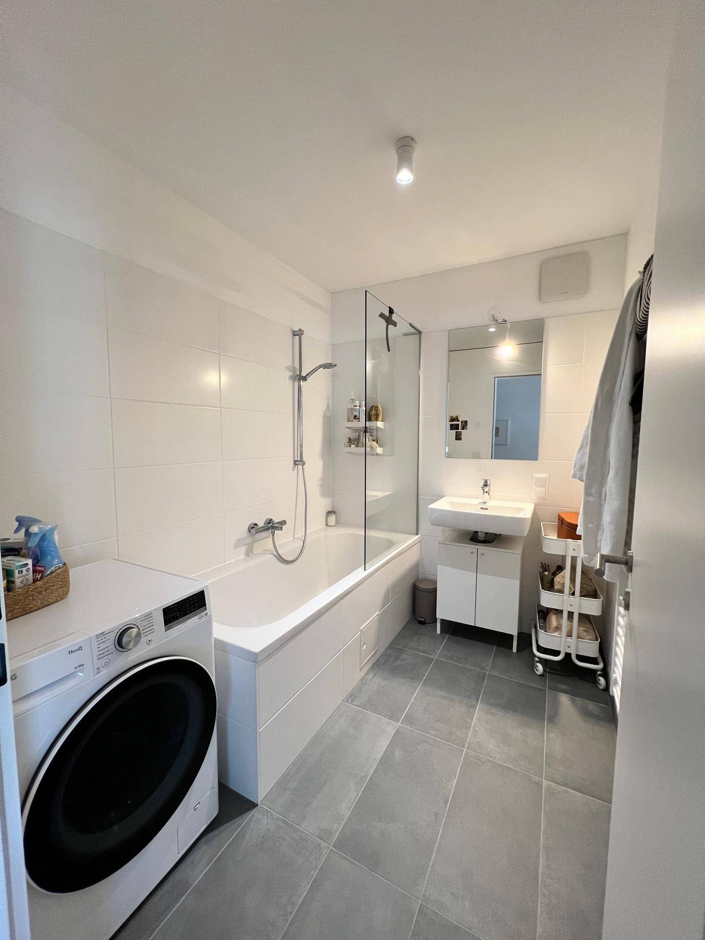 Modernes Badezimmer mit Badewanne, Dusche, Waschbecken und integrierter Waschmaschine.