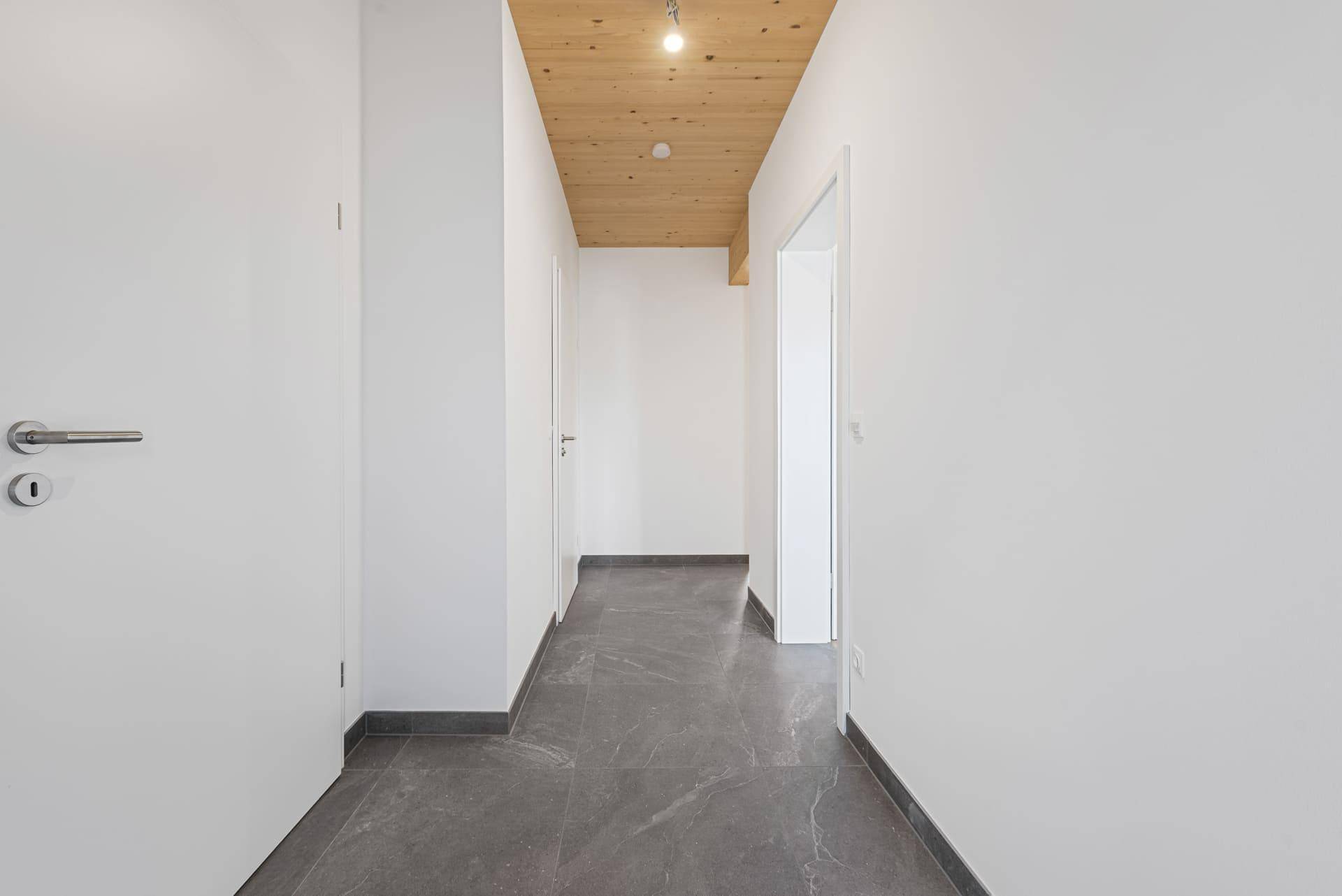 Heller Flur mit modernen grauen Fliesen und einer warmen Holzdecke.