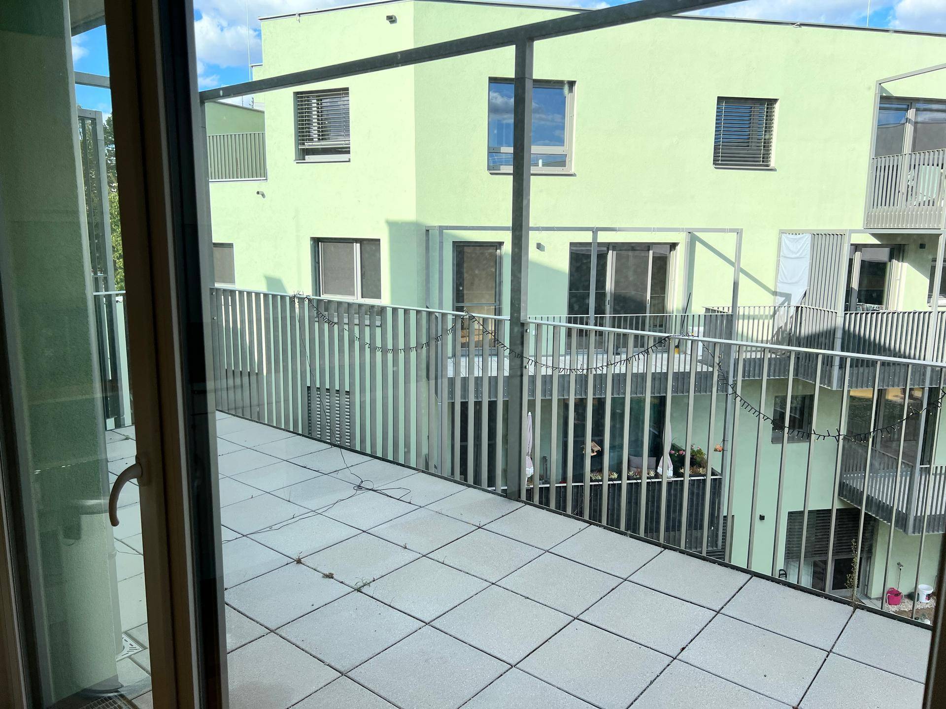 Geräumiger Balkon mit Fliesenboden und Blick auf die moderne Wohnanlage.
