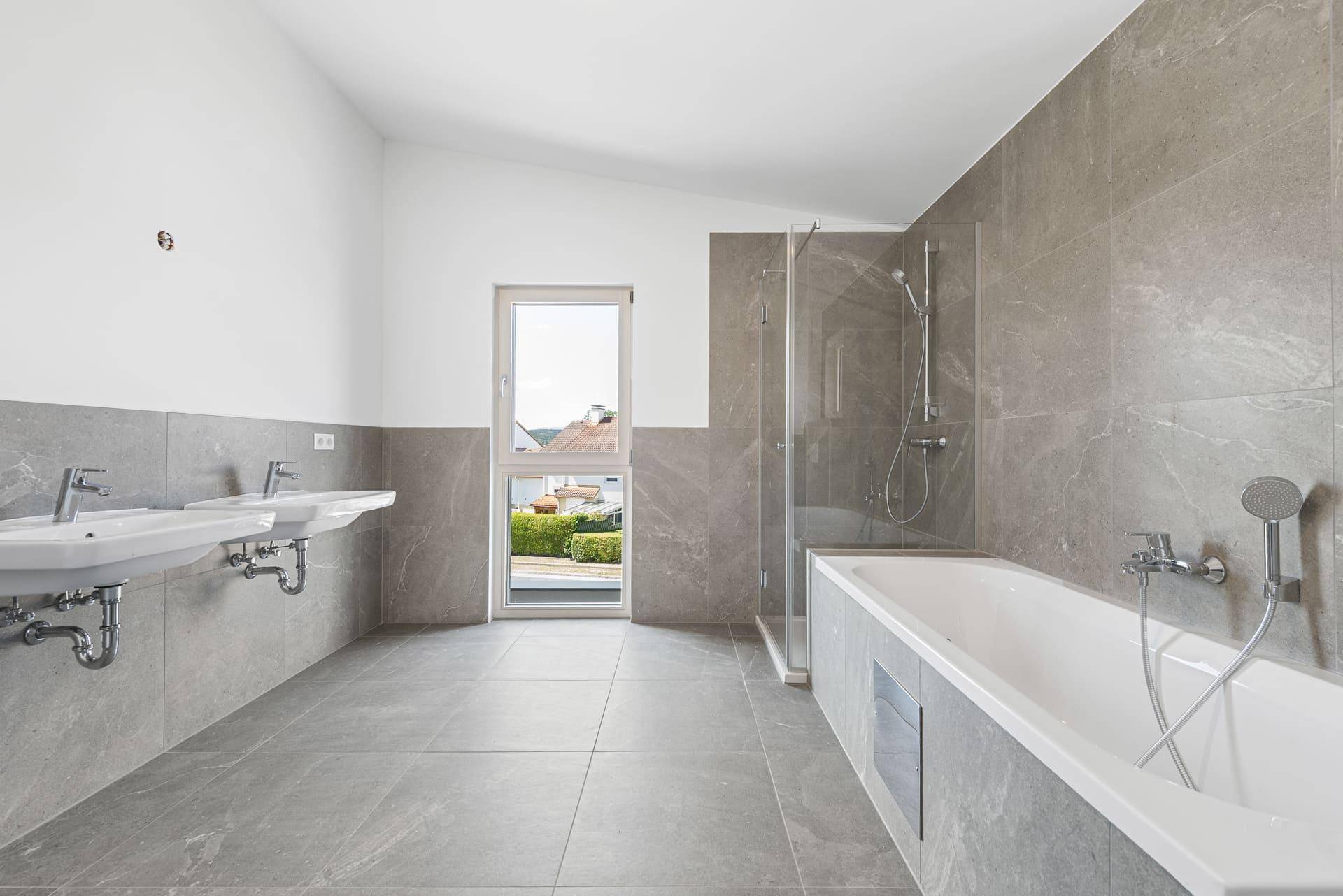 Geräumiges Badezimmer mit Badewanne, Dusche, Doppelwaschbecken und Fenster mit Aussicht.
