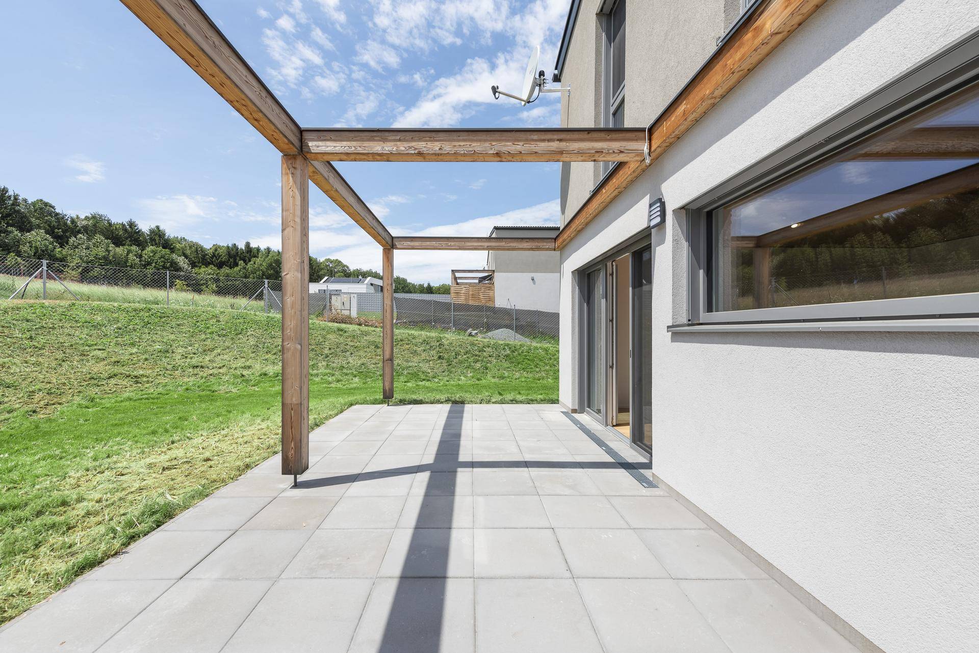 Weitläufige Terrasse mit moderner Holzpergola und Blick auf die umliegende Natur.