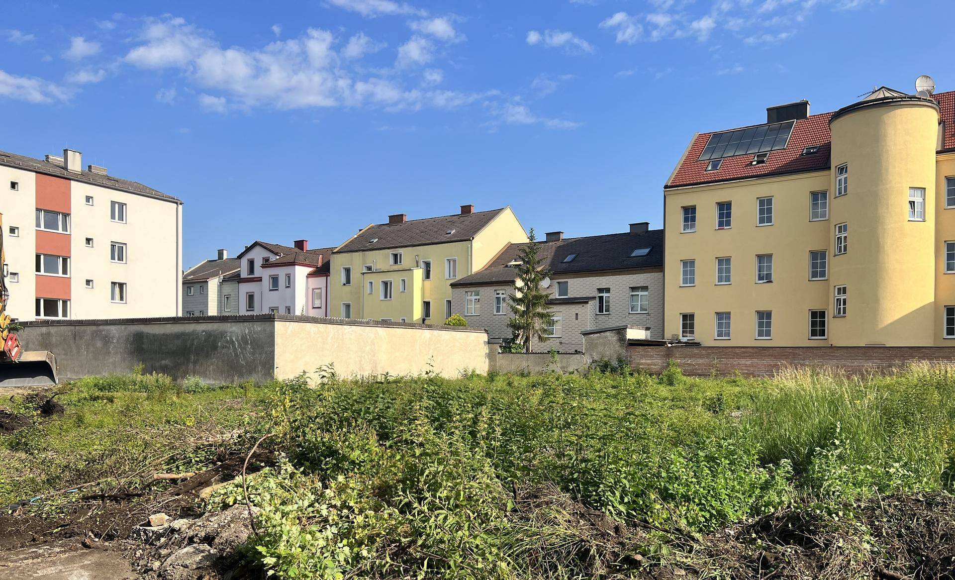 Blick auf ein unbebautes Grundstück mit umliegenden Wohngebäuden unter blauem Himmel.