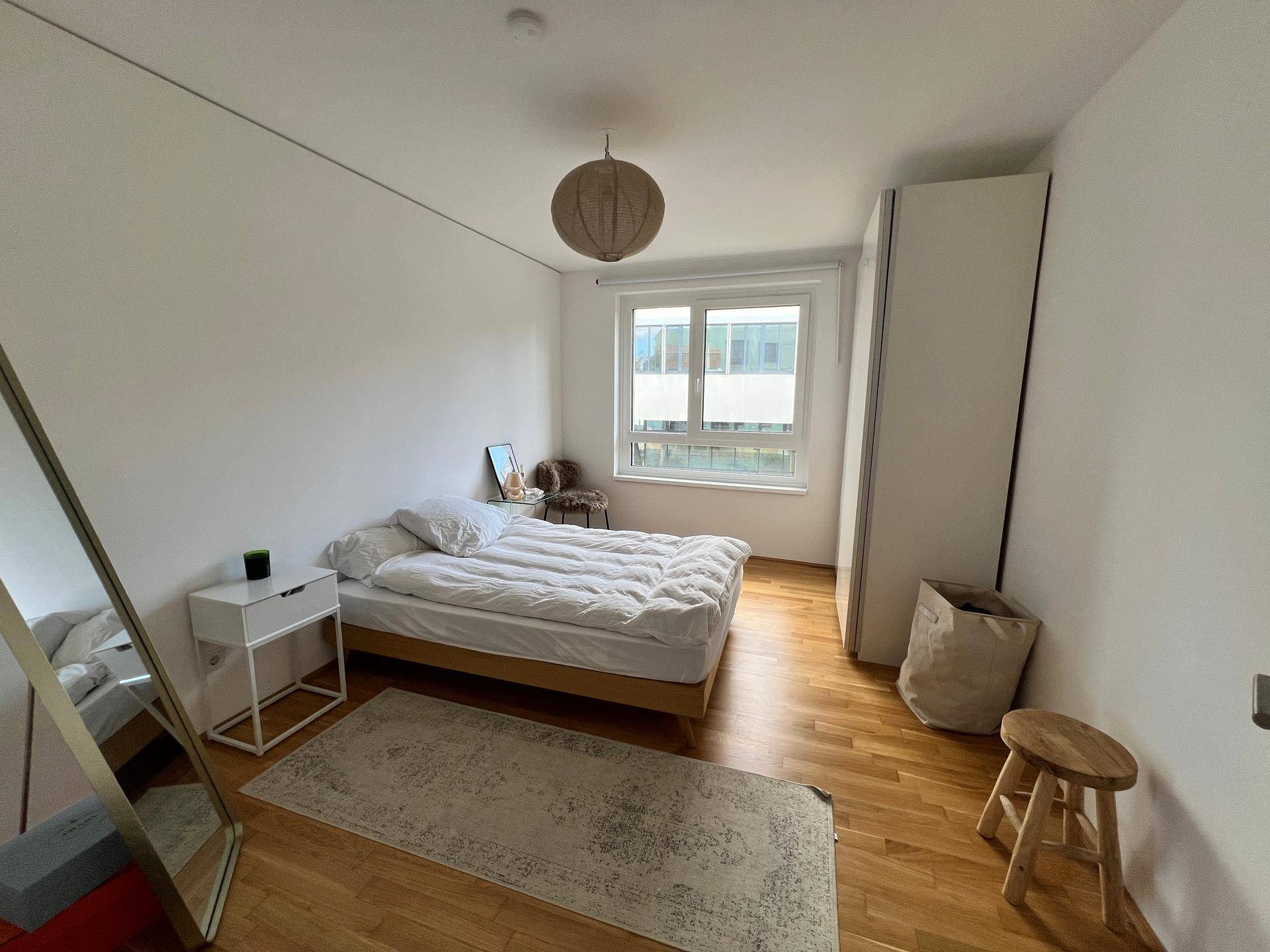 Gemütliches Schlafzimmer mit Holzboden, Bett und großem Fenster für natürliches Licht.