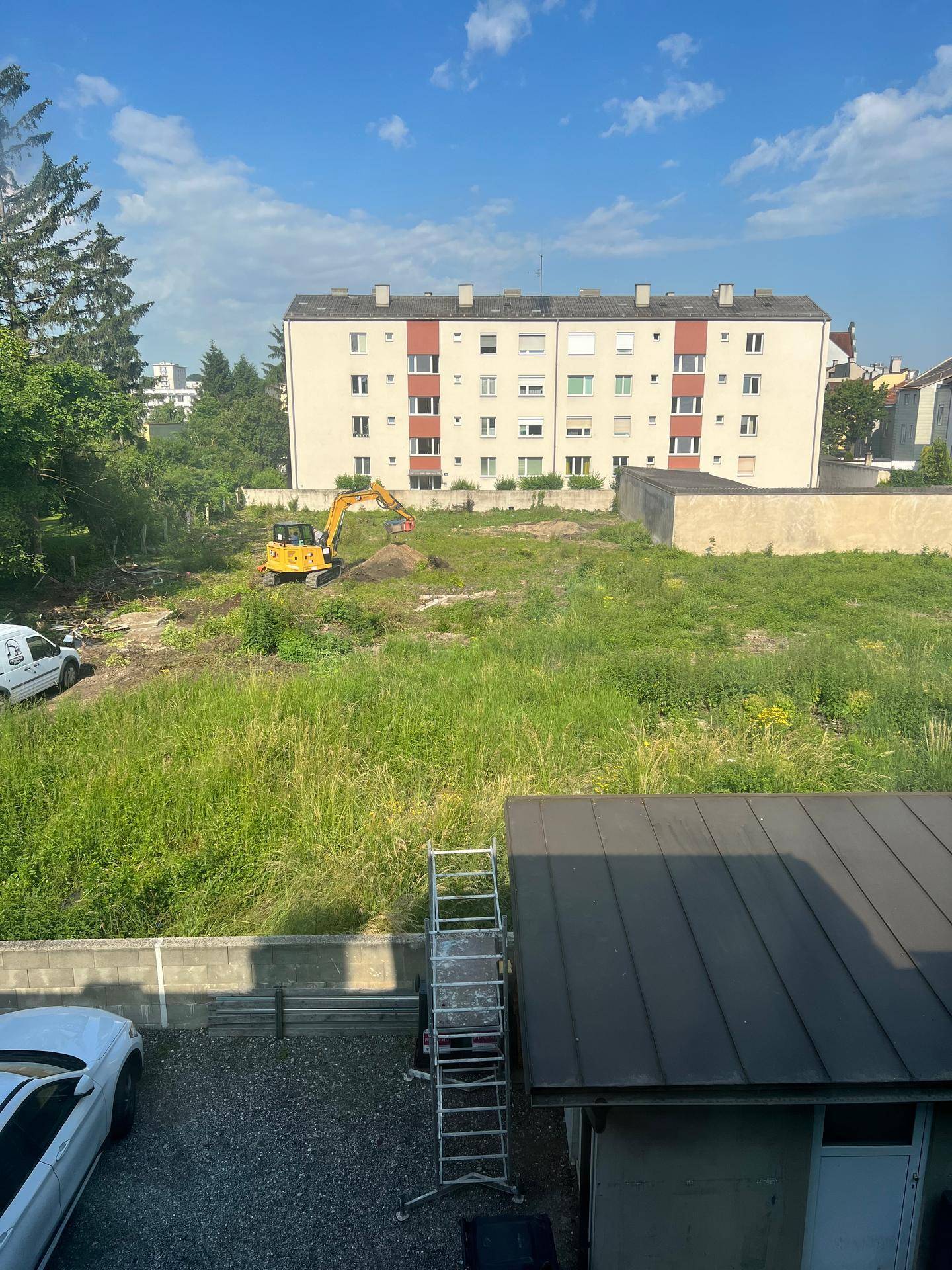 Übersicht über ein großes, unbebautes Grundstück mit Bagger und umliegenden Wohngebäuden.