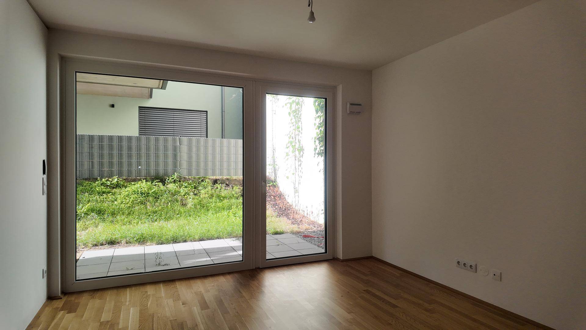 Heller Raum mit Holzboden und großen Schiebetüren, die den Blick auf den Außenbereich freigeben.