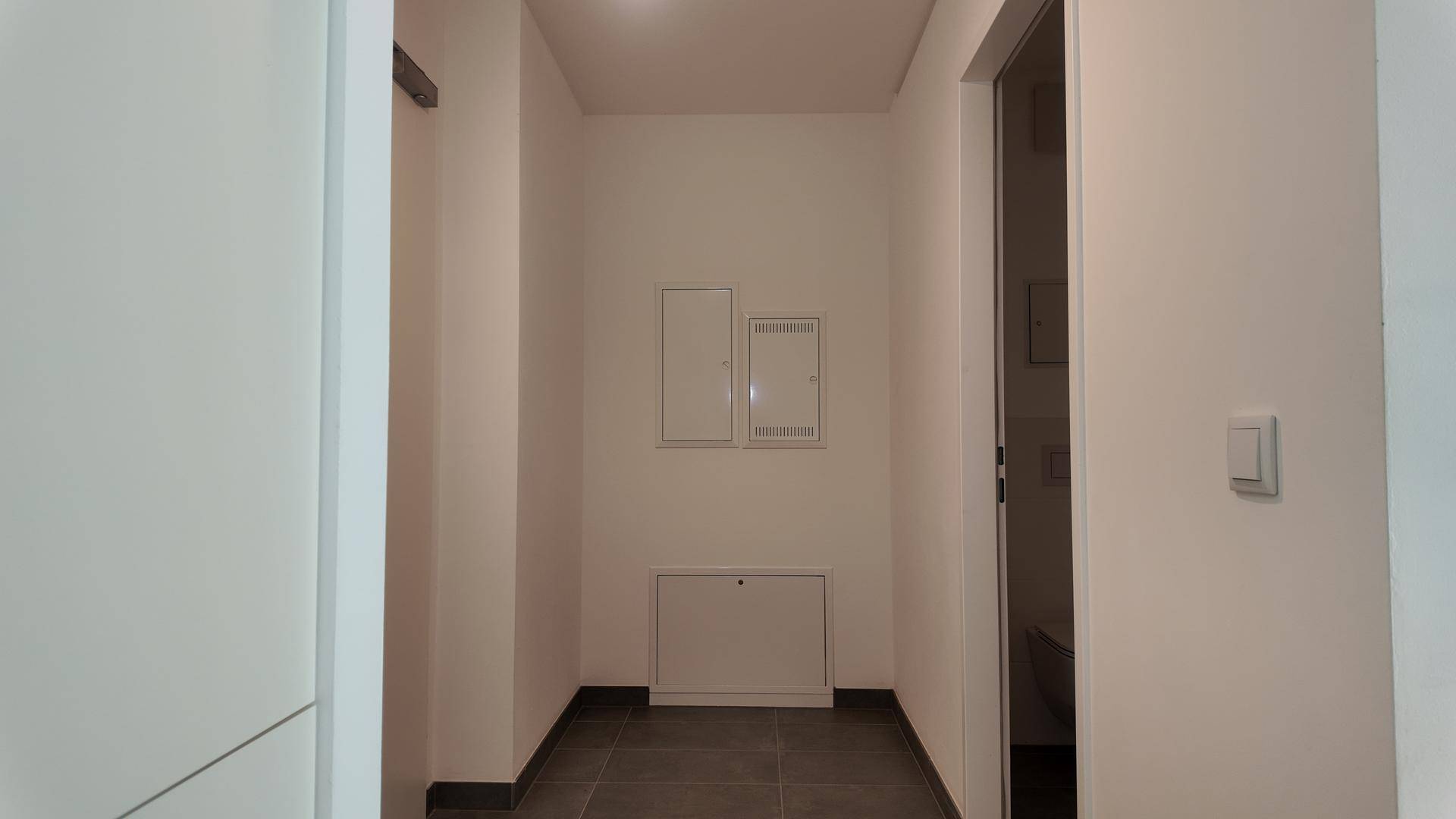 Heller Flur mit dunklen Fliesen und Wandpaneelen, der zu weiteren Räumen im Haus führt.