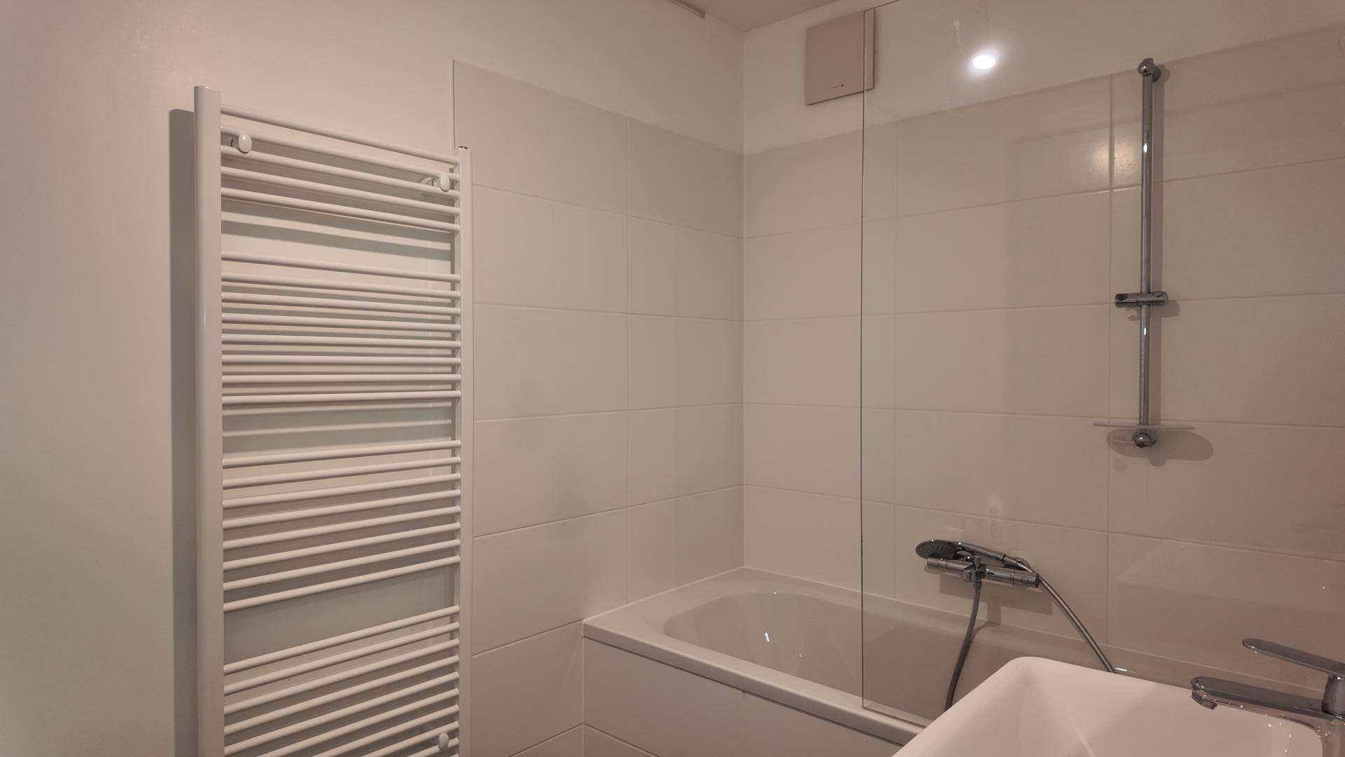 Modernes Badezimmer mit weißen Fliesen, Badewanne mit Duschwand und beheiztem Handtuchhalter.