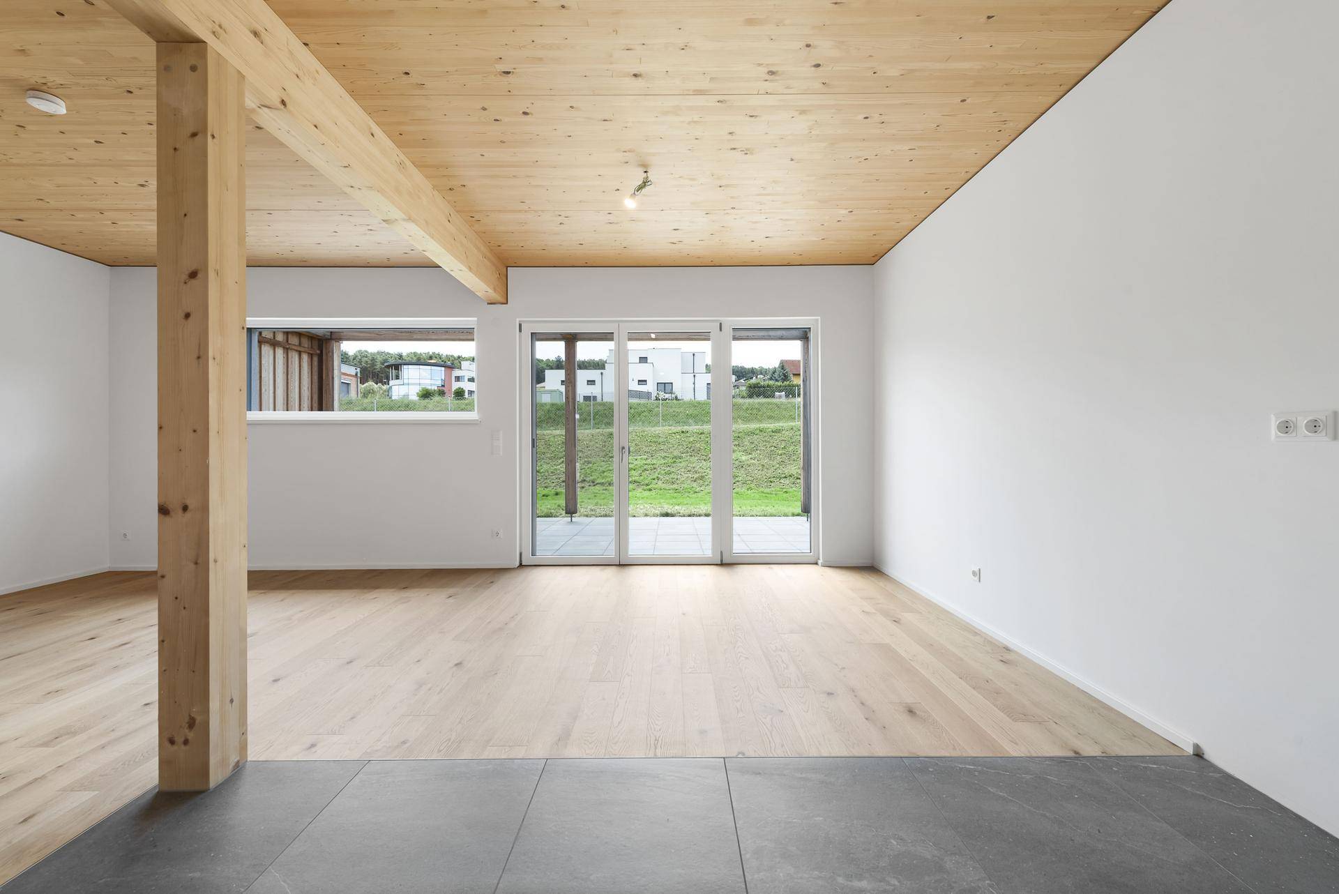 Geräumiger Wohnbereich mit Holzbalken, gemischtem Bodenbelag und großen Schiebetüren zum Garten.