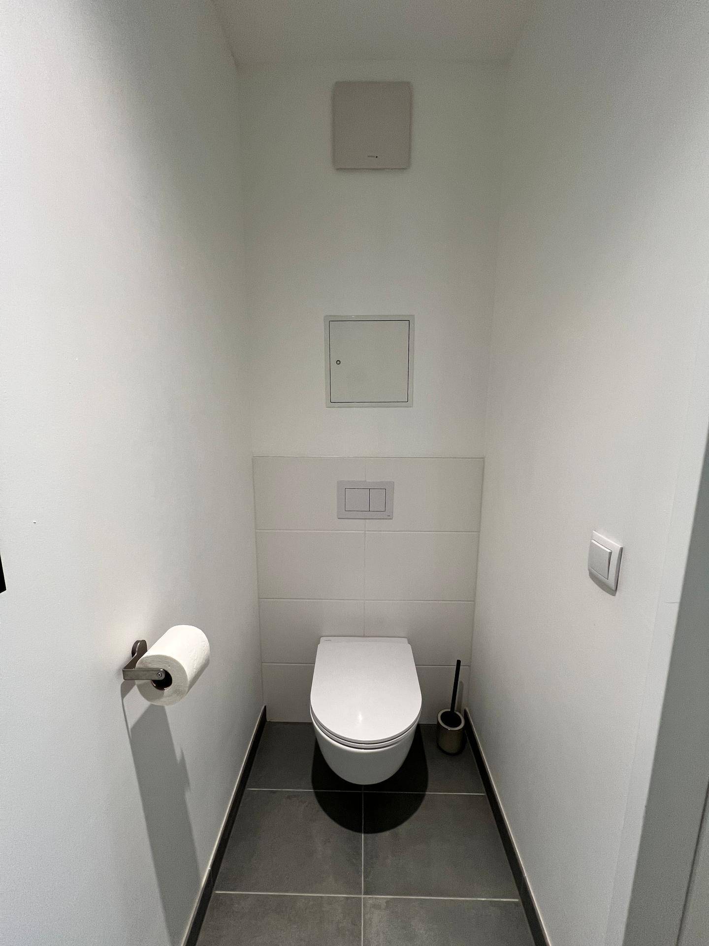 Sauberes Gäste-WC mit wandhängender Toilette und praktischer Abluftanlage.
