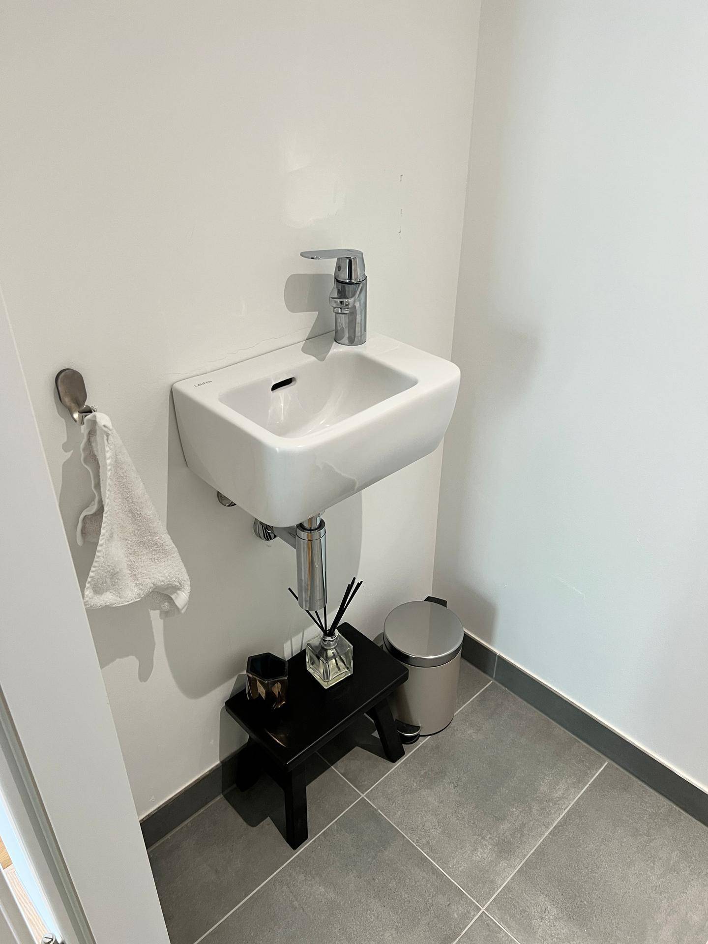 Modernes Gäste-WC mit wandhängendem Waschbecken und grauen Bodenfliesen.