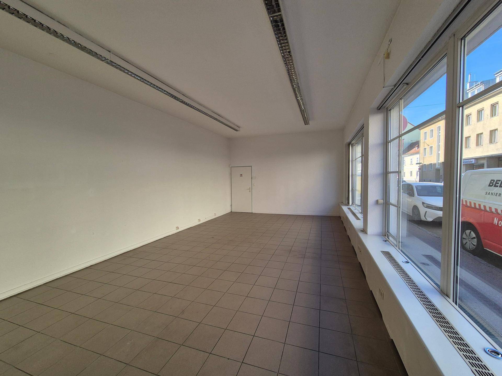 Geräumiger Gewerberaum mit großen Fenstern zur Straße und praktischem Fliesenboden.