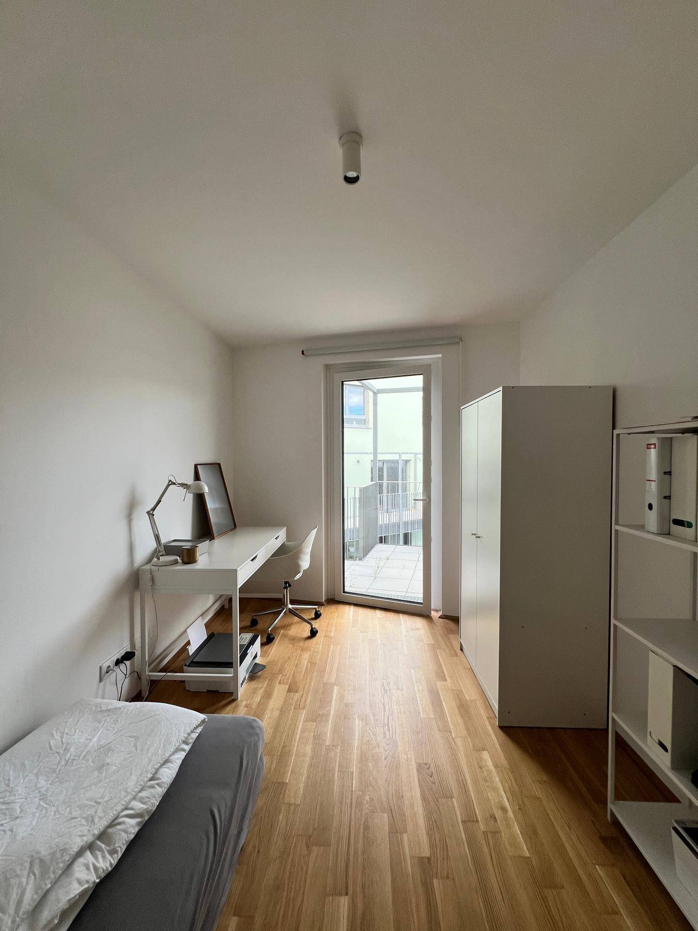 Helles Schlafzimmer oder Büro mit Schreibtisch, Bett und direktem Zugang zum Balkon.