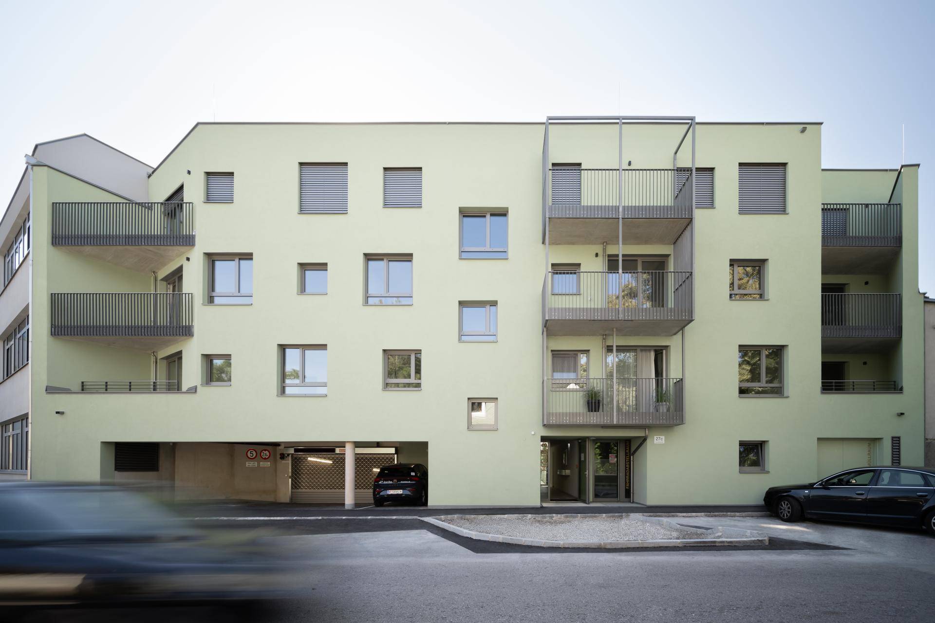 Moderne Wohnhausfassade in hellem Grün mit zahlreichen Balkonen und einer Tiefgaragenzufahrt.