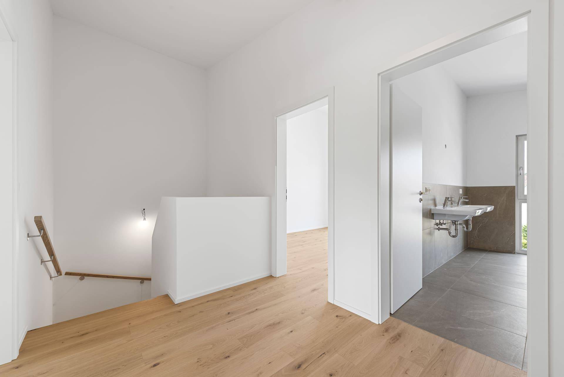 Heller Flur im Obergeschoss mit Holzboden und Blick auf das Badezimmer und die Treppe.