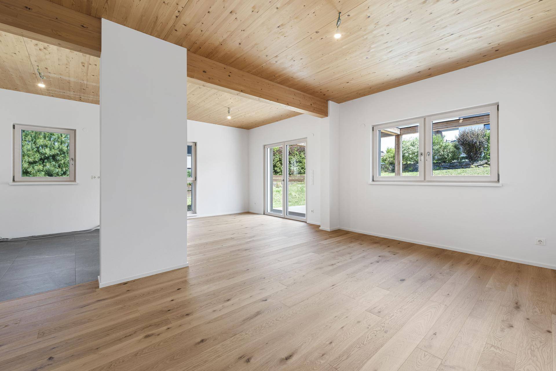 Geräumiger offener Wohnbereich mit Holzboden, Holzdecke und Zugang zum Garten.