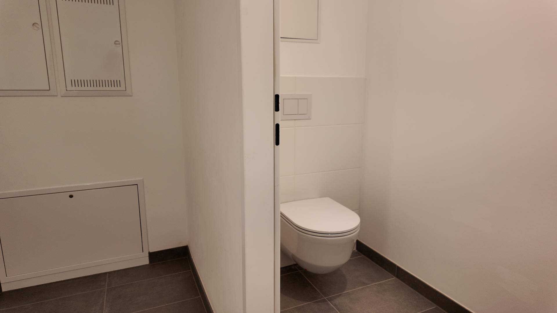 Kleines Gäste-WC mit wandhängender Toilette und dunklem Fliesenboden, praktisch und funktional.