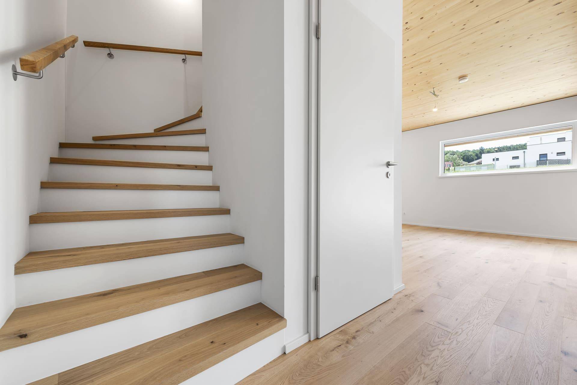 Helle Holztreppe mit schlichtem Design und Holzbalkendecke, die zum oberen Stockwerk führt.