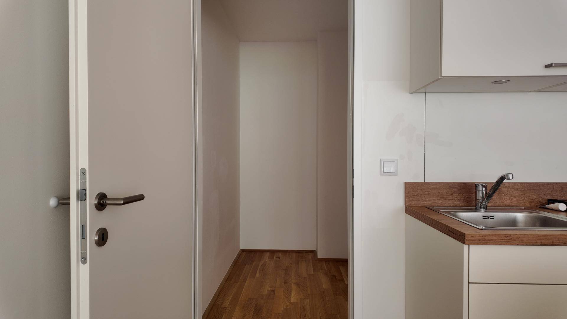 Küchenbereich mit Spülbecken aus Edelstahl, Holz-Arbeitsplatte und einer Tür zu einem Nebenraum.