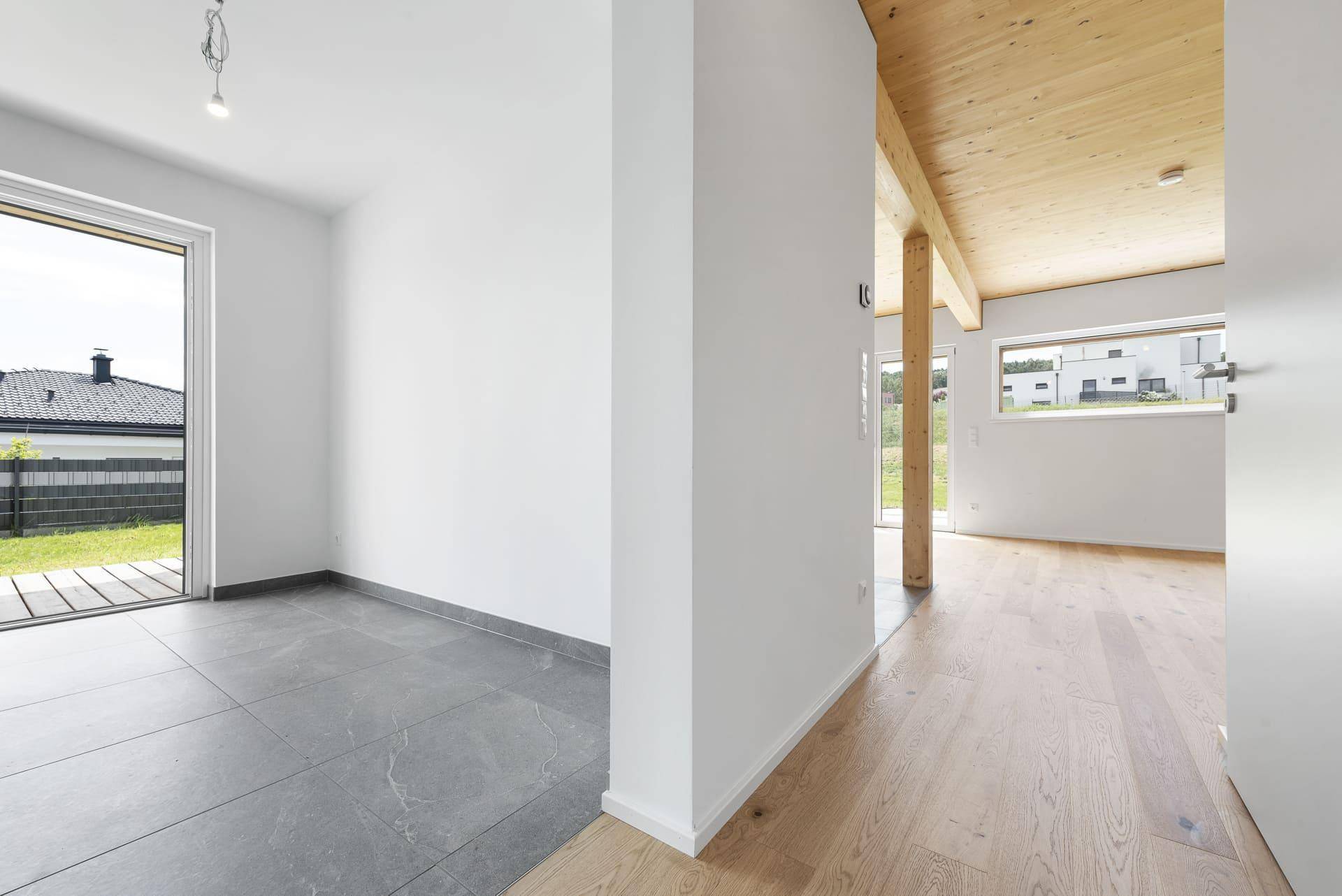 Offener Wohnbereich mit Holzbalkendecke, gemischtem Bodenbelag und Zugang zum Garten.