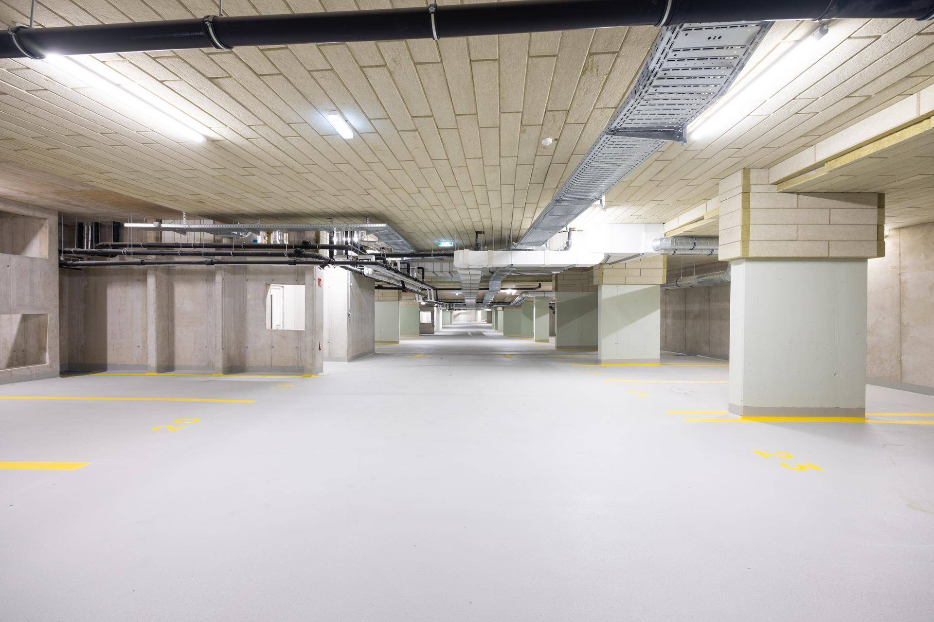 Helle und saubere Tiefgarage mit Betonstützen und Deckeninstallationen für eine gute Beleuchtung.