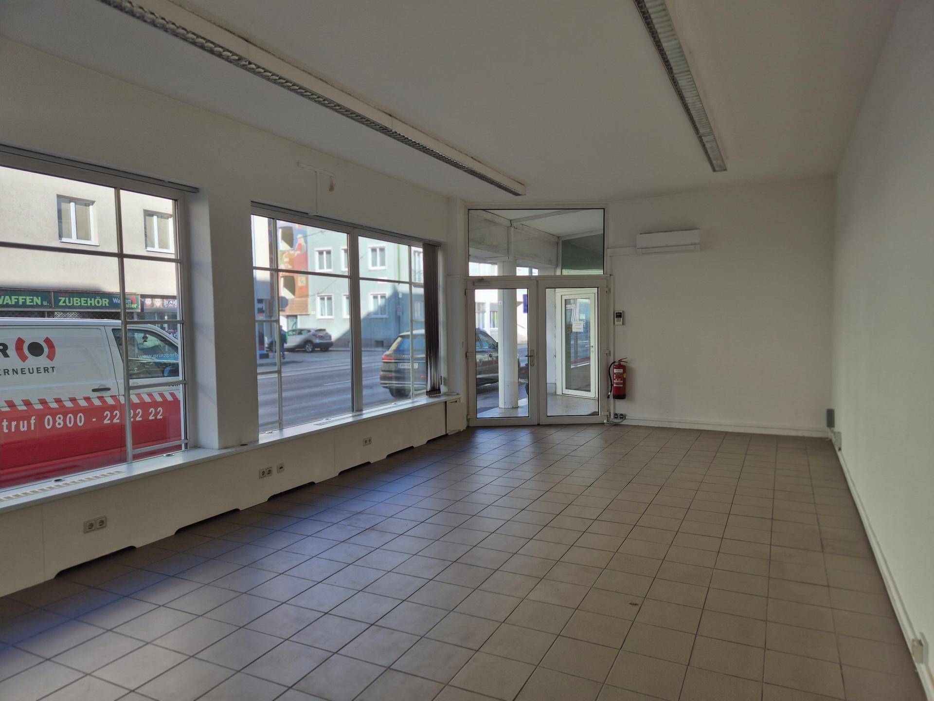 Offener Gewerberaum mit viel Tageslicht durch die großen Fensterfronten und Zugangstür.