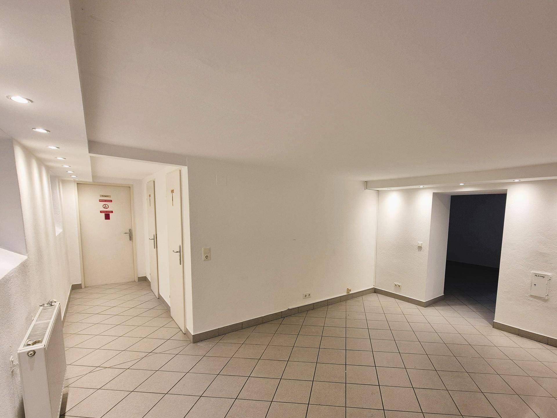 Heller Flur mit Fliesenboden und mehreren Türen, beleuchtet durch Deckenspots.