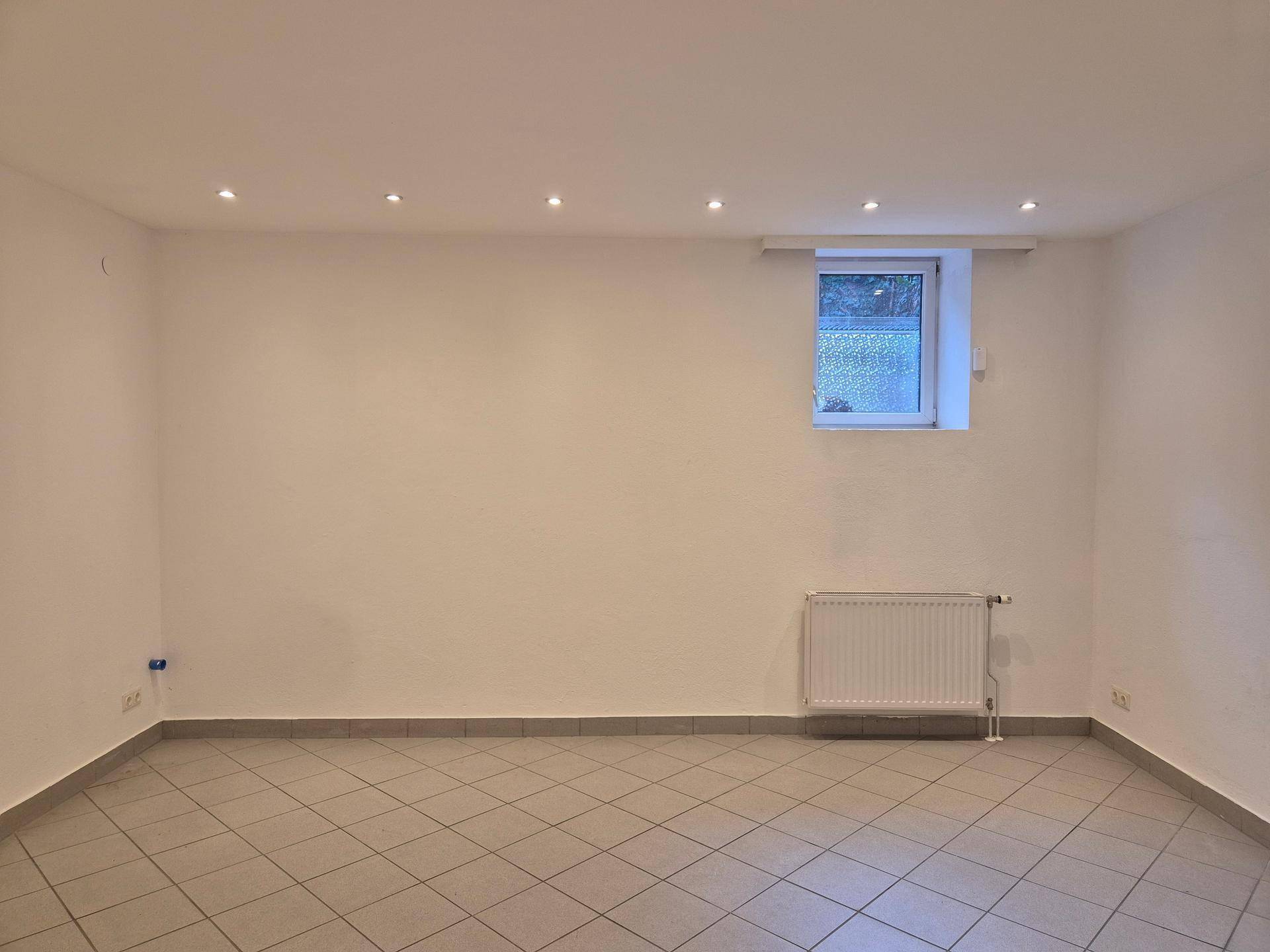 Einfacher Raum im Untergeschoss mit kleinem Fenster, Heizkörper und Deckenspots.