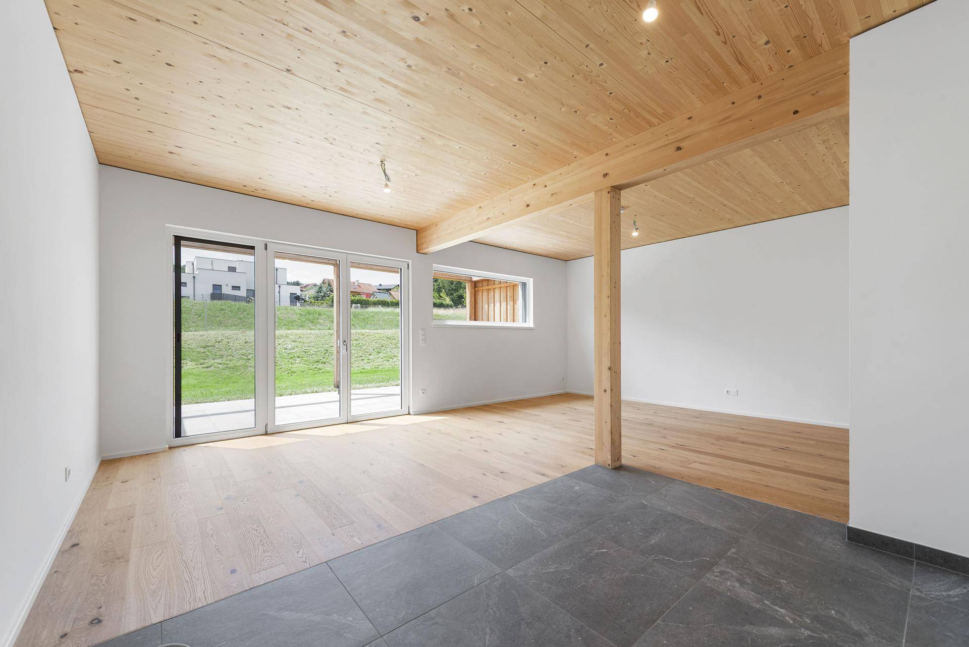 Großzügiger Wohnraum mit Holzbalkendecke, unterschiedlichen Bodenbelägen und viel Tageslicht.