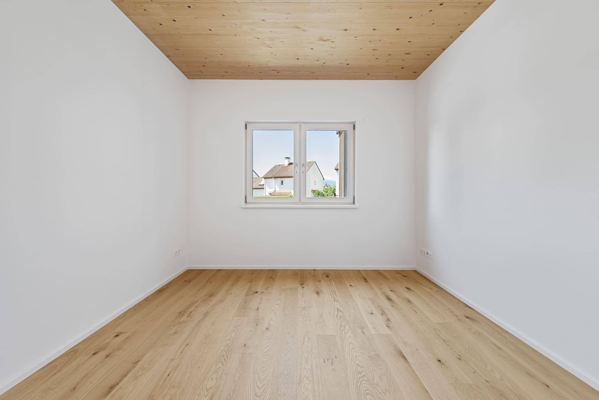 Helles Zimmer mit Holzboden, Holzdecke und Blick auf die umliegenden Häuser.