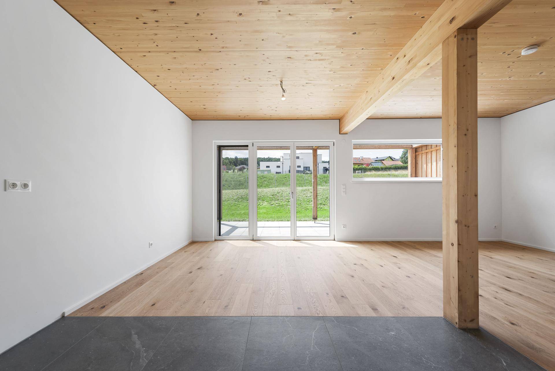 Heller und offener Wohnbereich mit Holzbalkendecke und direktem Zugang zur Terrasse und zum Garten.