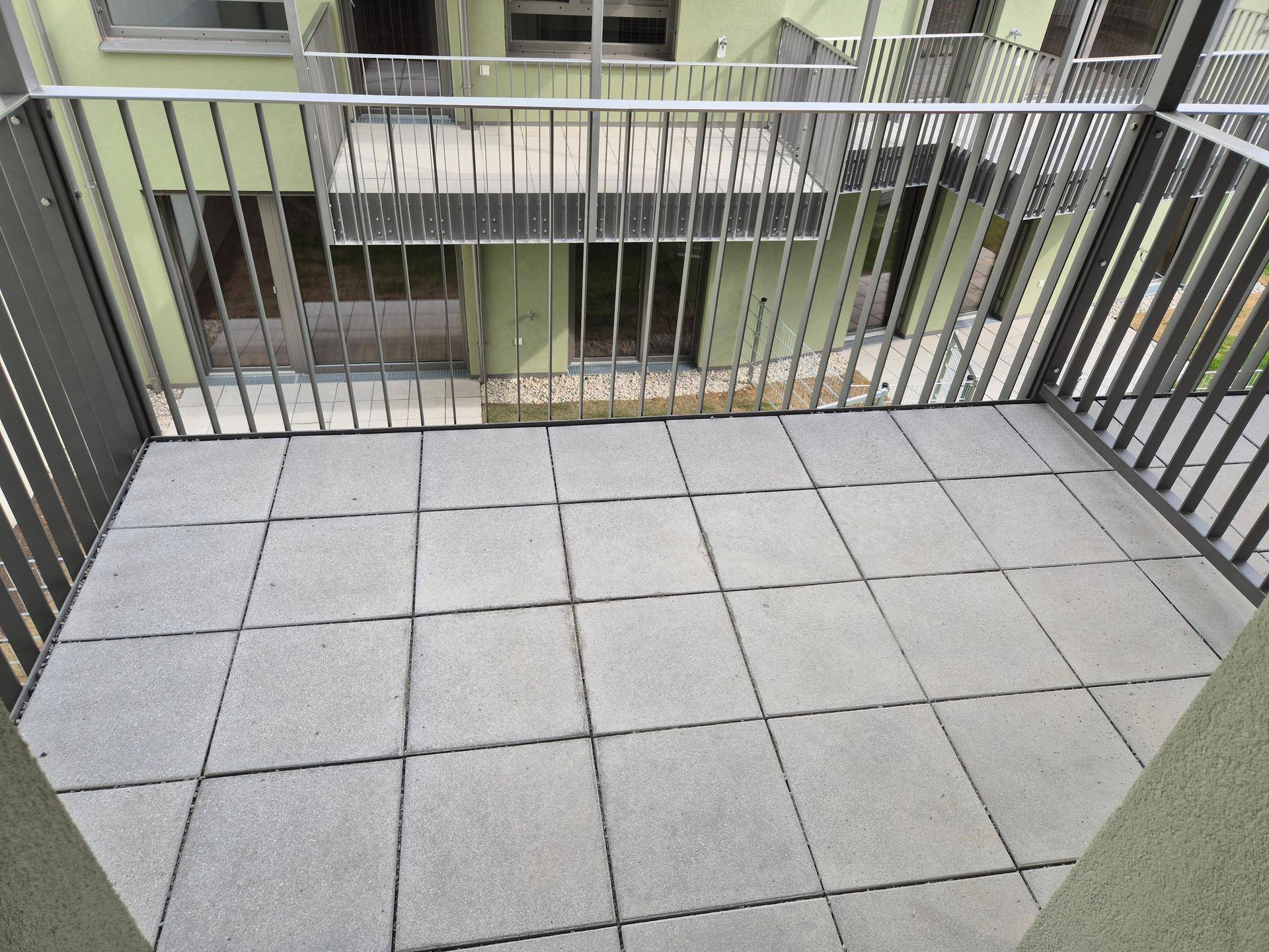 Balkon mit Fliesenboden und Metallgeländer, bietet einen Blick auf den begrünten Innenhof.