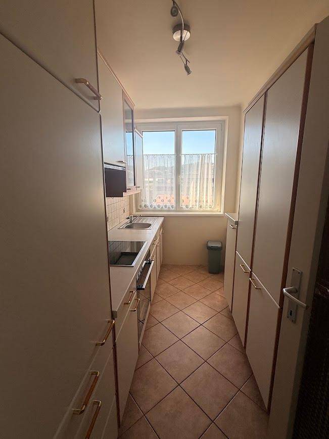 Funktionale Küche mit weißen Schränken, Fliesenboden und Fenster für Tageslicht.