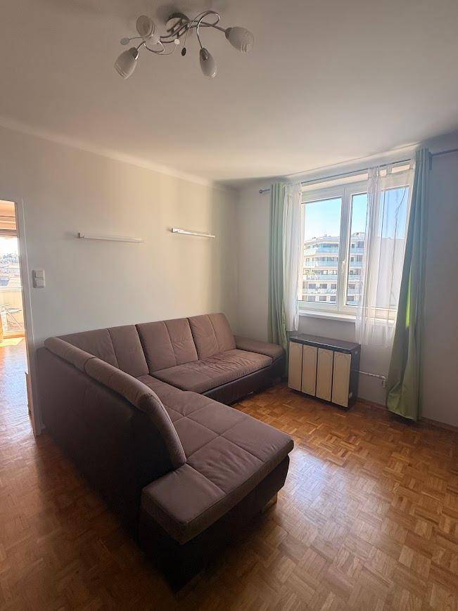Helles Wohnzimmer mit braunem Ecksofa, Parkettboden und Blick nach draußen.