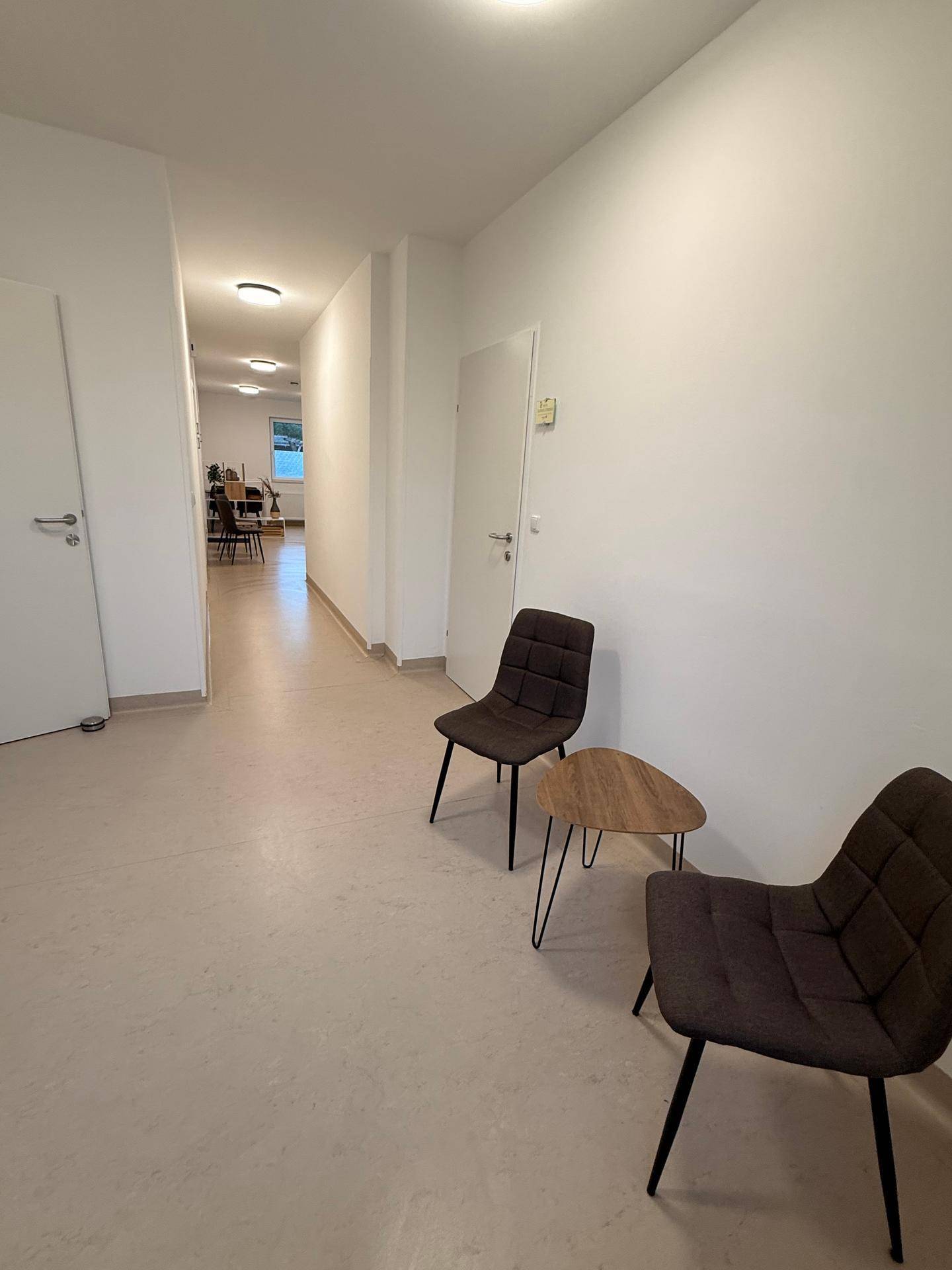 Langer, heller Flur mit Sitzgelegenheiten und mehreren Türen zu angrenzenden Räumen.
