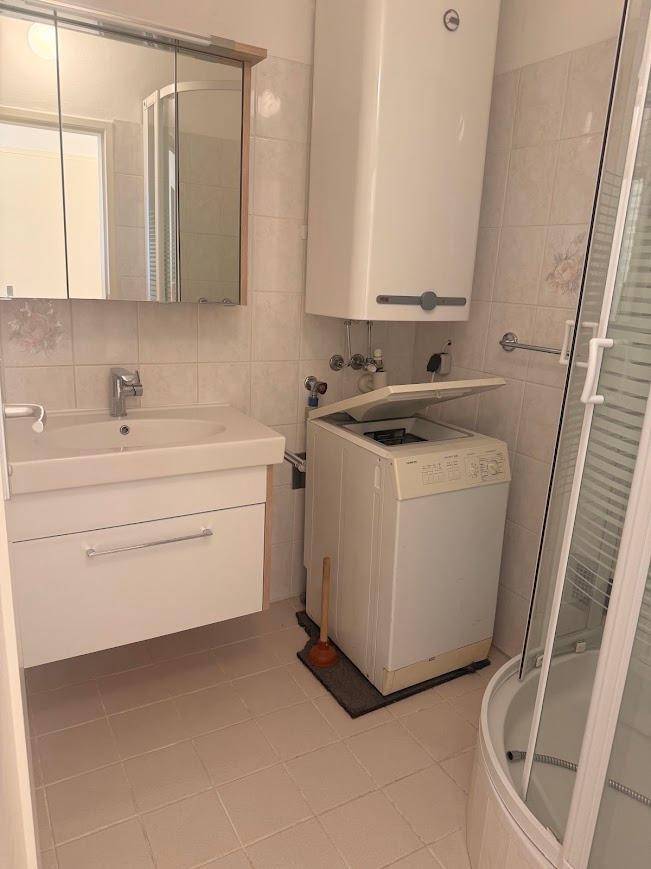 Badezimmer mit Waschbecken, Duschkabine und integrierter Waschmaschine.