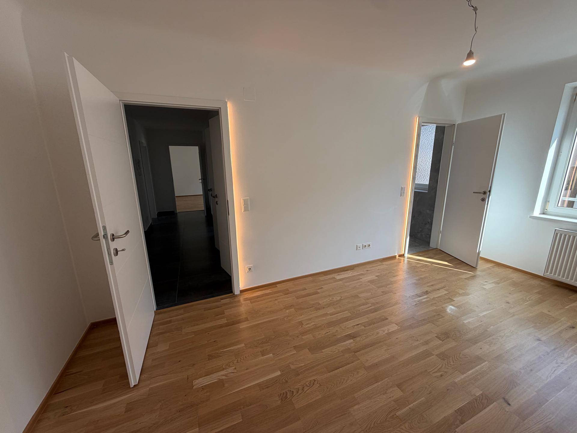 Helles Schlafzimmer mit Parkettboden und weißen Wänden, einladend und bereit zur individuellen Gestaltung.