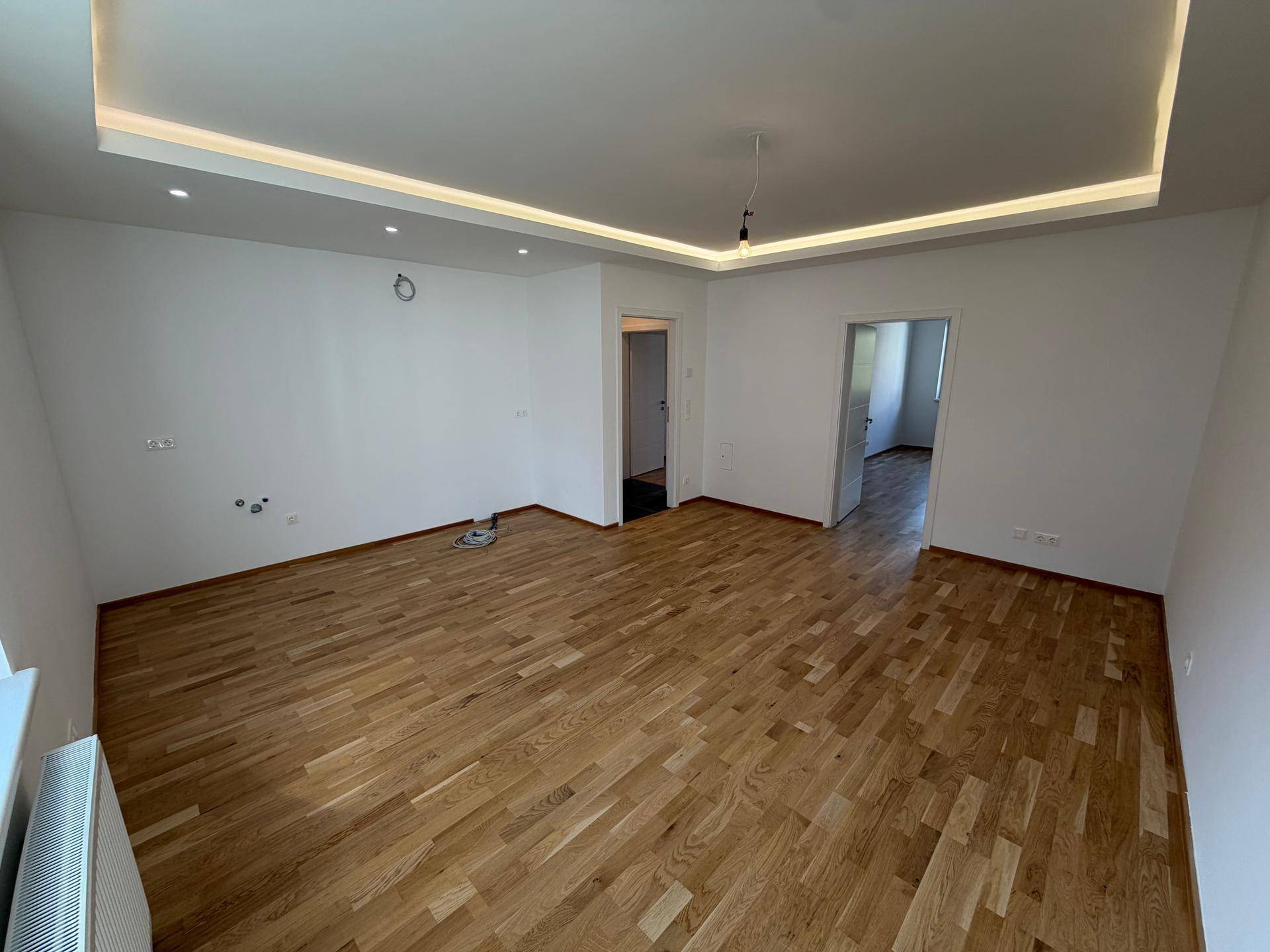 Helles Wohnzimmer mit Eichenparkett, weißen Wänden und indirekter Deckenbeleuchtung, bereit zur Einrichtung.