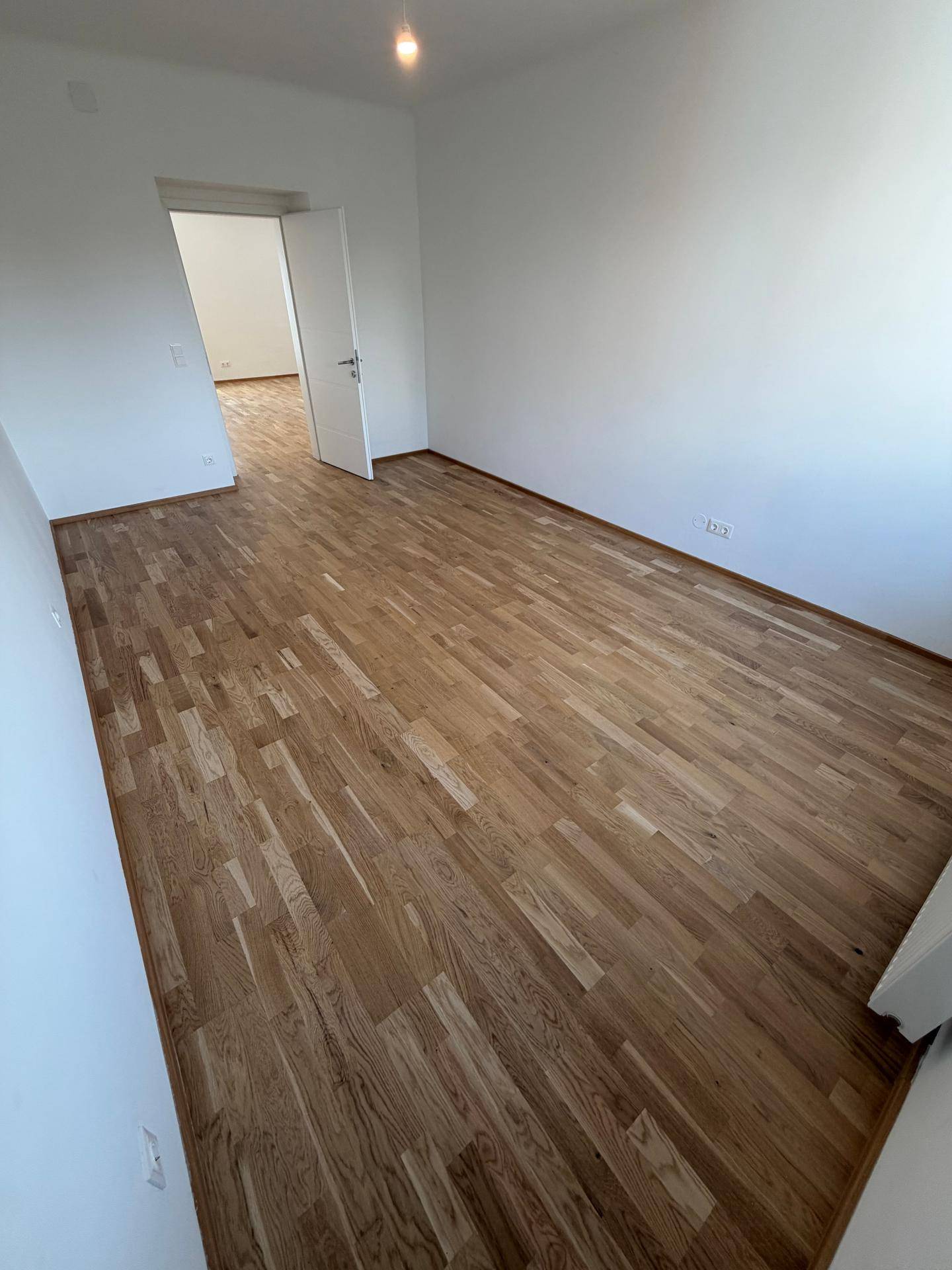 Geräumiges, helles Zimmer mit Parkettboden und weißen Wänden, bietet vielseitige Nutzungsmöglichkeiten.